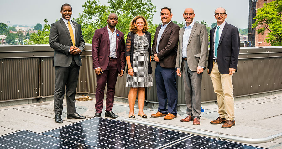 People standing next to solar panels on apartment rooftop