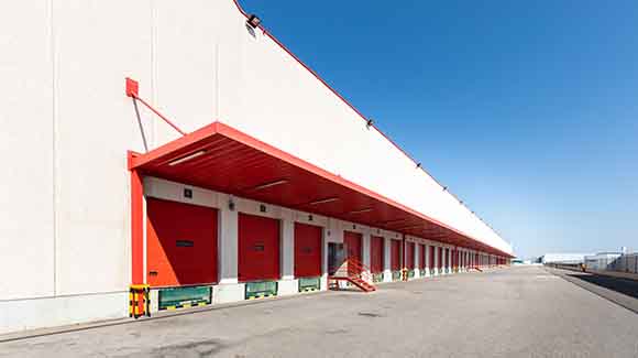 Truck bays with red doors and red overhang on white logistics building