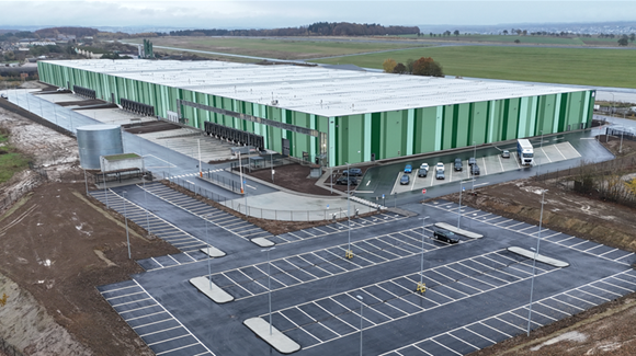 Aerial of large green striped industrial bilding with truck bays and a large parking lot