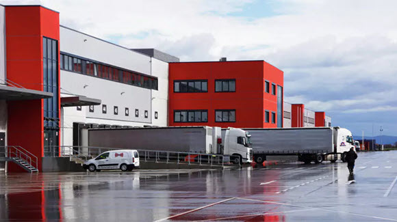 Close-up photo of a red and white multi-story industrial building with two trucks