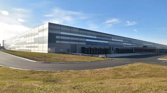 Photo of a large patterened industrial building with truck bays on one side