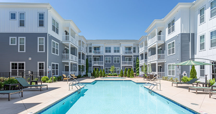 Three-story grey and white multifamily community complex with a pool