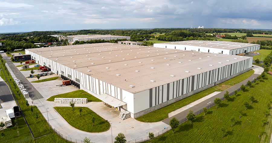 Aerial of large striped grey and white industrial warehouse surrounded by green fields