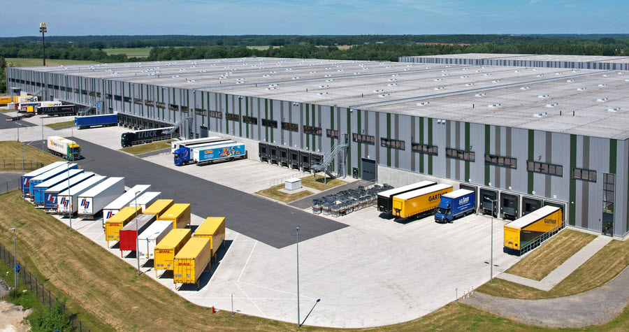 Large grey industrial warehouse with multiple large trucks in the loading dock