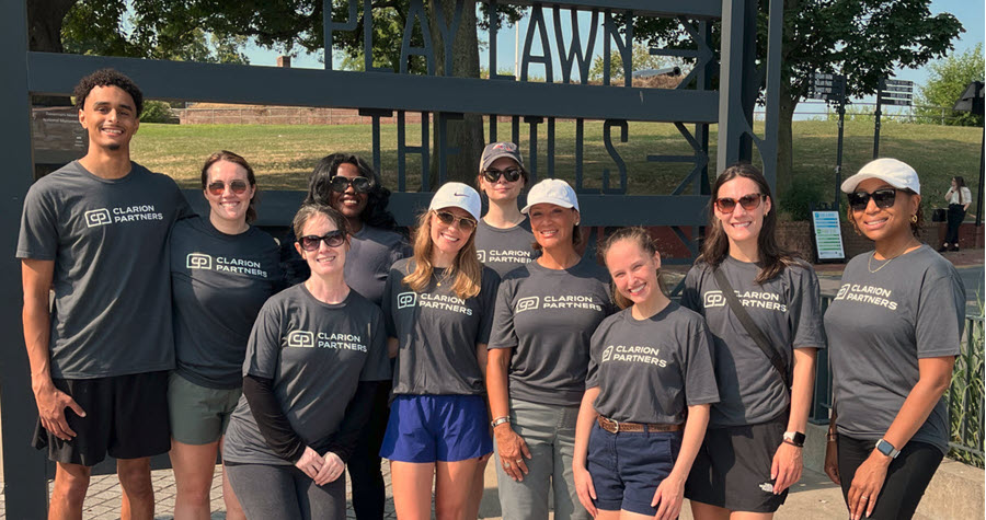 Photo of a group of Clarion employees wearing company shirts in front of a sign on Governor's Island