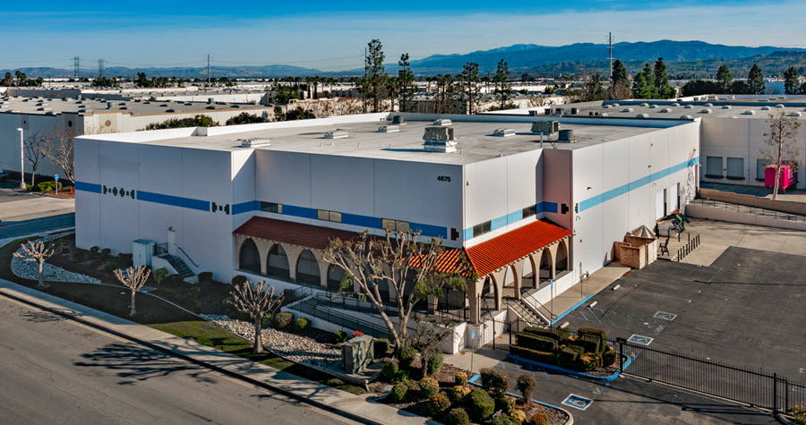 Industrial warehouse with red-roof covered terrace awning and small parking lot and shrubbery