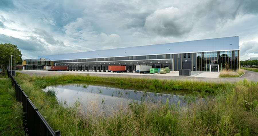 Tall industrial warehouse with small pond, grass and black fencing